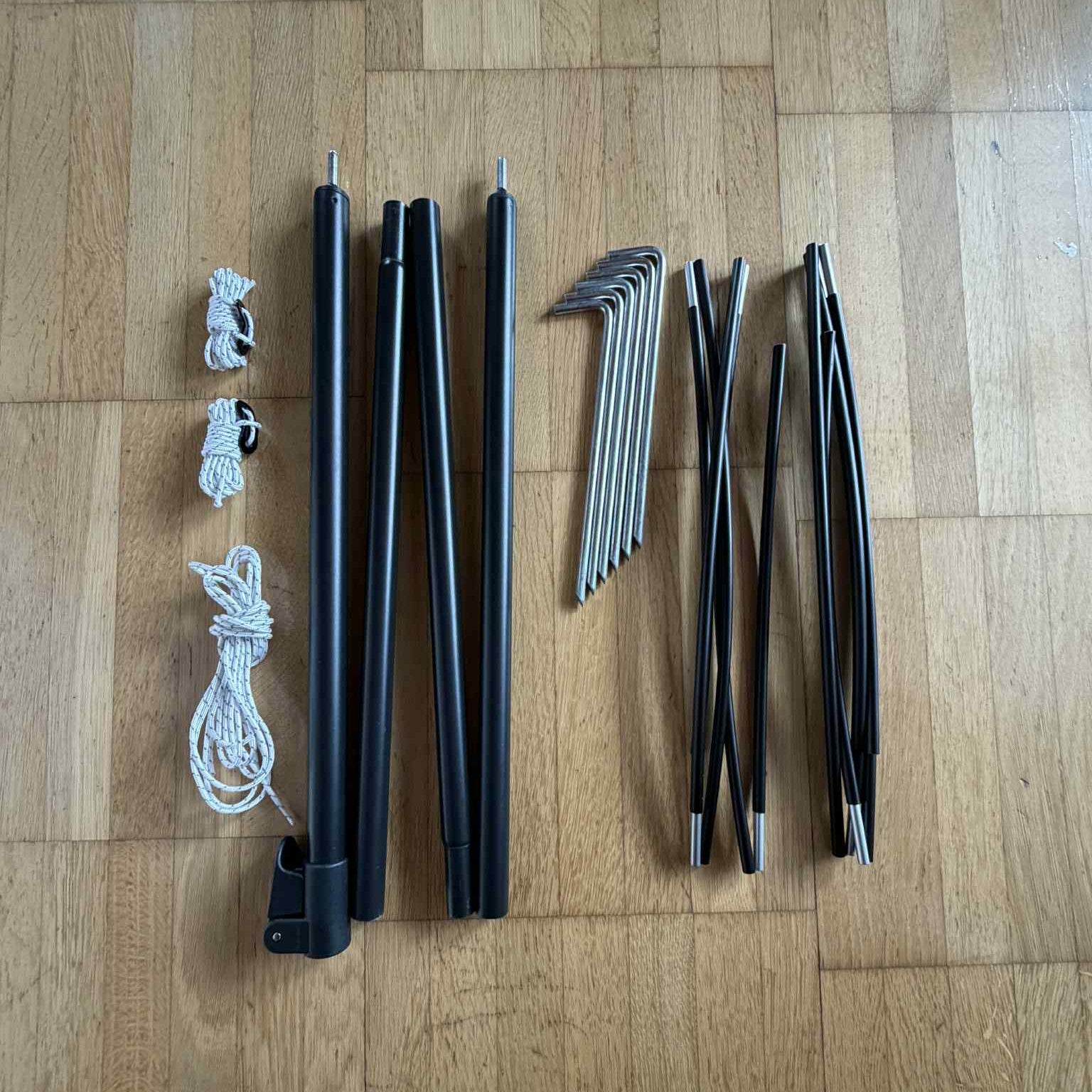 Black tent poles, ropes, and metal stakes on a wooden floor